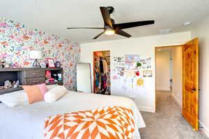 Bedroom featuring wallpapered walls, a spacious closet, carpet flooring, a textured ceiling, and a closet