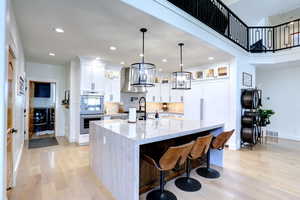 Kitchen with double oven, range hood, light wood-style flooring, a large island with sink, and recessed lighting