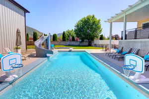 View of pool featuring a water slide, a patio, a fenced backyard, and a mountain view