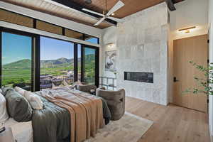 Bedroom featuring wood finished floors, a mountain view, a tiled fireplace, a wooden ceiling with exposed beams, and a high ceiling