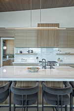 Kitchen featuring decorative backsplash, a kitchen breakfast bar, light stone counters, wall chimney range hood, and wood ceiling
