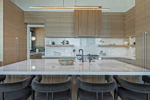 Kitchen featuring open shelves, modern cabinets, a kitchen bar, and light stone countertops