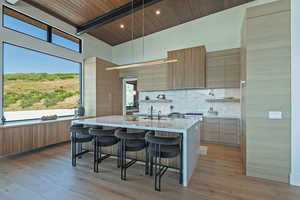 Kitchen featuring modern cabinets, a breakfast bar area, decorative backsplash, a wood ceiling with exposed beams, and high vaulted ceiling