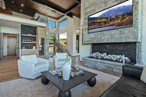 Living area with high vaulted ceiling, a wooden ceiling with exposed beams, wood finished floors, stairway, and a stone fireplace