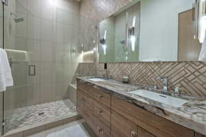 Bathroom with double vanity, a shower stall, and tasteful backsplash