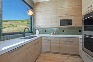 Kitchen featuring black microwave, double oven, decorative backsplash, light stone counters, and light wood-style floors