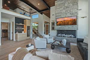 Living room with a high ceiling, a fireplace, a wood ceiling with exposed beams, wood finished floors, and stairs