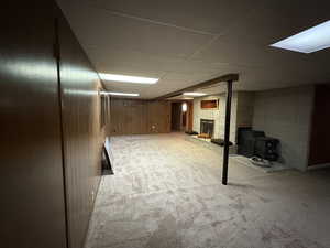 Finished below grade area featuring a drop ceiling, carpet, a brick fireplace, wood walls, and a wood stove