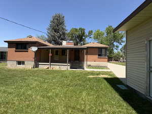 Rear view of house with brick siding, a porch, a yard, roof with shingles, and a chimney