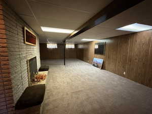 Basement with a paneled ceiling, carpet flooring, a fireplace, and wood walls