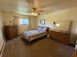 Bedroom featuring baseboard heating, dark colored carpet, and a ceiling fan