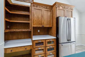 Kitchen featuring freestanding refrigerator, lofted ceiling, light tile patterned floors, brown cabinets, and light countertops