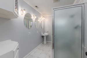 Full bathroom with marble finish floors, crown molding, and a shower stall
