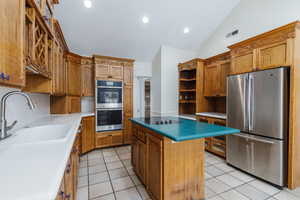 Kitchen featuring appliances with stainless steel finishes, open shelves, light tile patterned flooring, decorative backsplash, and vaulted ceiling