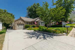 Ranch-style house featuring an attached garage, stone siding, driveway, and a front yard