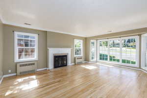 Unfurnished living room with radiator heating unit, ornamental molding, wood finished floors, and a fireplace with flush hearth