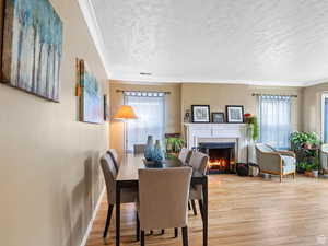 Dining area featuring a lit fireplace, a textured ceiling, wood finished floors, and crown molding