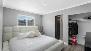 Bedroom with crown molding, a textured ceiling, wood finished floors, and a closet