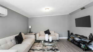 Living area with wood finished floors, a wall unit AC, a textured ceiling, and crown molding