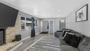Living room featuring a textured ceiling, arched walkways, light wood-style flooring, recessed lighting, and a fireplace with raised hearth