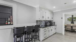 Kitchen featuring stainless steel microwave, white cabinets, dark countertops, tasteful backsplash, and crown molding