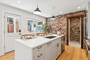 Kitchen featuring brick wall, stainless steel dishwasher, light wood finished floors, decorative light fixtures, and light countertops