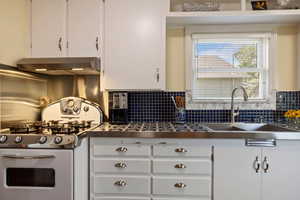 Kitchen featuring stainless steel gas range oven, wall chimney exhaust hood, white cabinetry, and backsplash