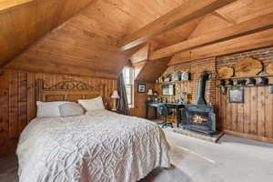 Bedroom featuring carpet floors, wood ceiling, wood walls, and a wood stove