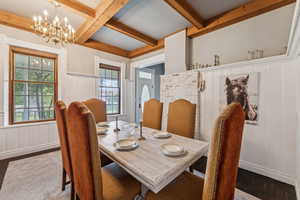 Dining area with wood finished floors, a decorative wall, beamed ceiling, a chandelier, and coffered ceiling