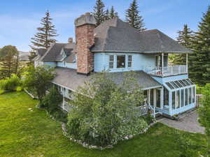 Rear view of property featuring a chimney, a balcony, a sunroom, a shingled roof, and a lawn