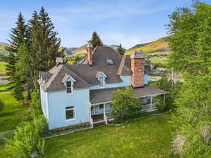Back of house with a chimney, a lawn, a shingled roof, a porch, and a mountain view