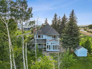 Back of property with a balcony, a chimney, a shingled roof, a sunroom, and a lawn