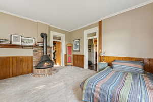 Carpeted bedroom with a wood stove, a wainscoted wall, crown molding, and wood walls