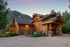 Log home featuring gravel driveway, stone siding, a garage, a mountain view, and a shingled roof