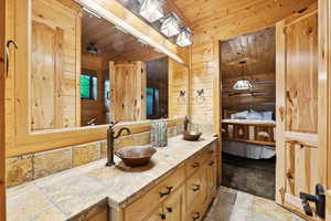 Full bathroom featuring stone tile floors, double vanity, wood ceiling, wooden walls, and ensuite bathroom
