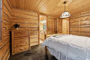 Bedroom with carpet floors, wooden ceiling, wood walls, and connected bathroom