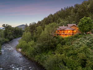 Back of property at dusk featuring a chimney, a view of trees, log siding, and a wooden deck
