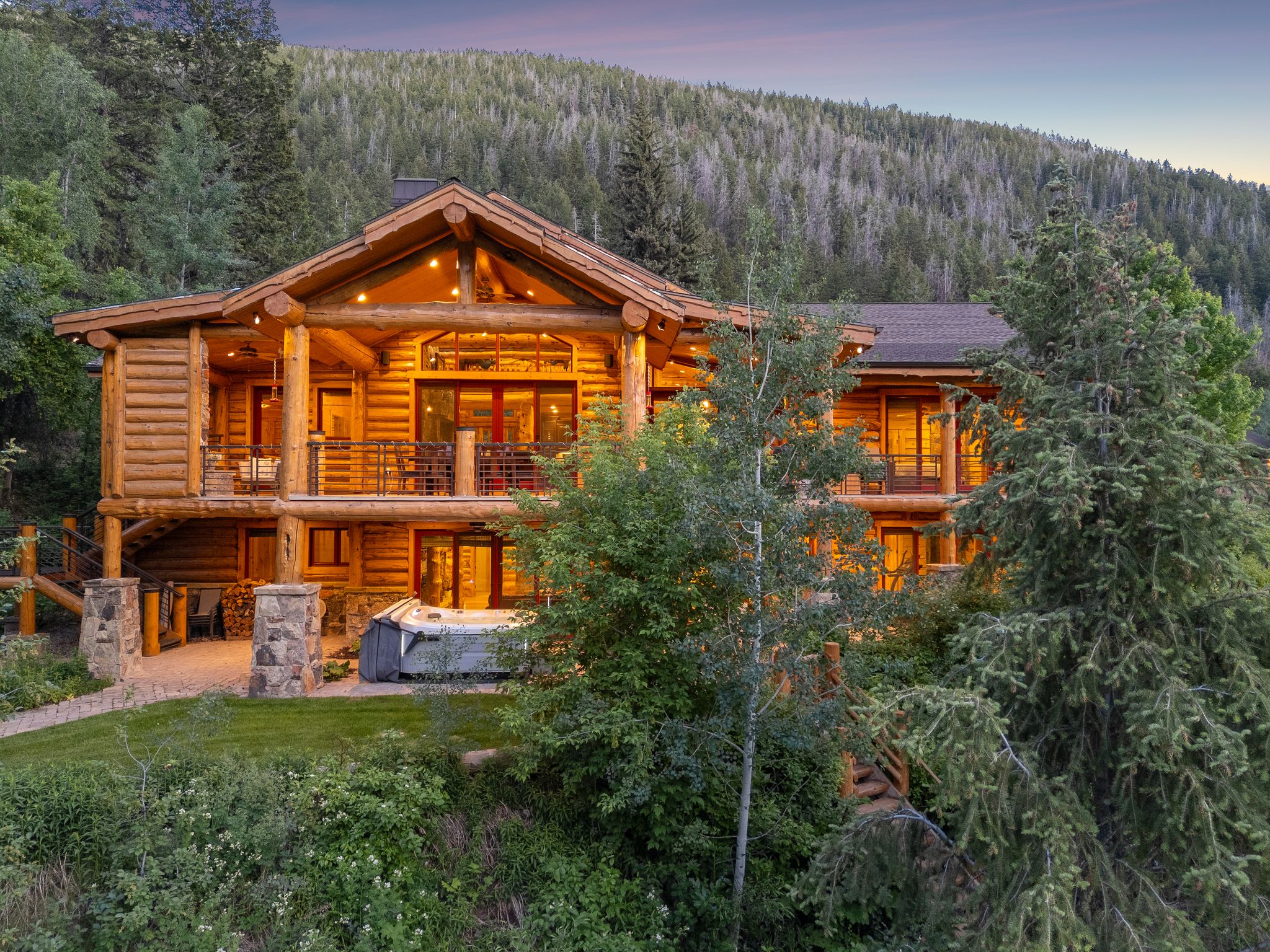 Back of property featuring a forest view, split-log veneer framed home, a balcony, and a patio