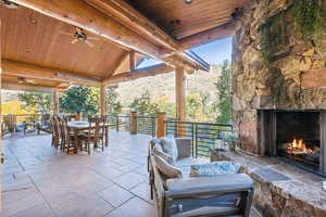 View of patio / terrace with ceiling fan, outdoor dining area, an outdoor stone fireplace, and a mountain view