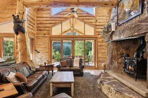 Living room with log walls, high vaulted ceiling, a wood stove, and beamed ceiling