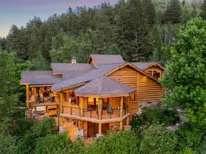Back of property with a balcony, a shingled roof, stone siding, a chimney, and log exterior