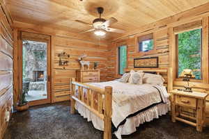 Bedroom with wooden ceiling, dark colored carpet, access to outside, wooden walls, and a fireplace