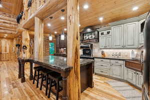 Kitchen with log walls, wooden ceiling, light wood-style floors, a breakfast bar area, and a kitchen island