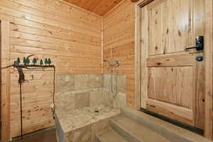 Bathroom with wood ceiling, tiled shower, and wooden walls