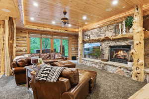 Living room featuring wood ceiling, log walls, a fireplace, ceiling fan, and recessed lighting