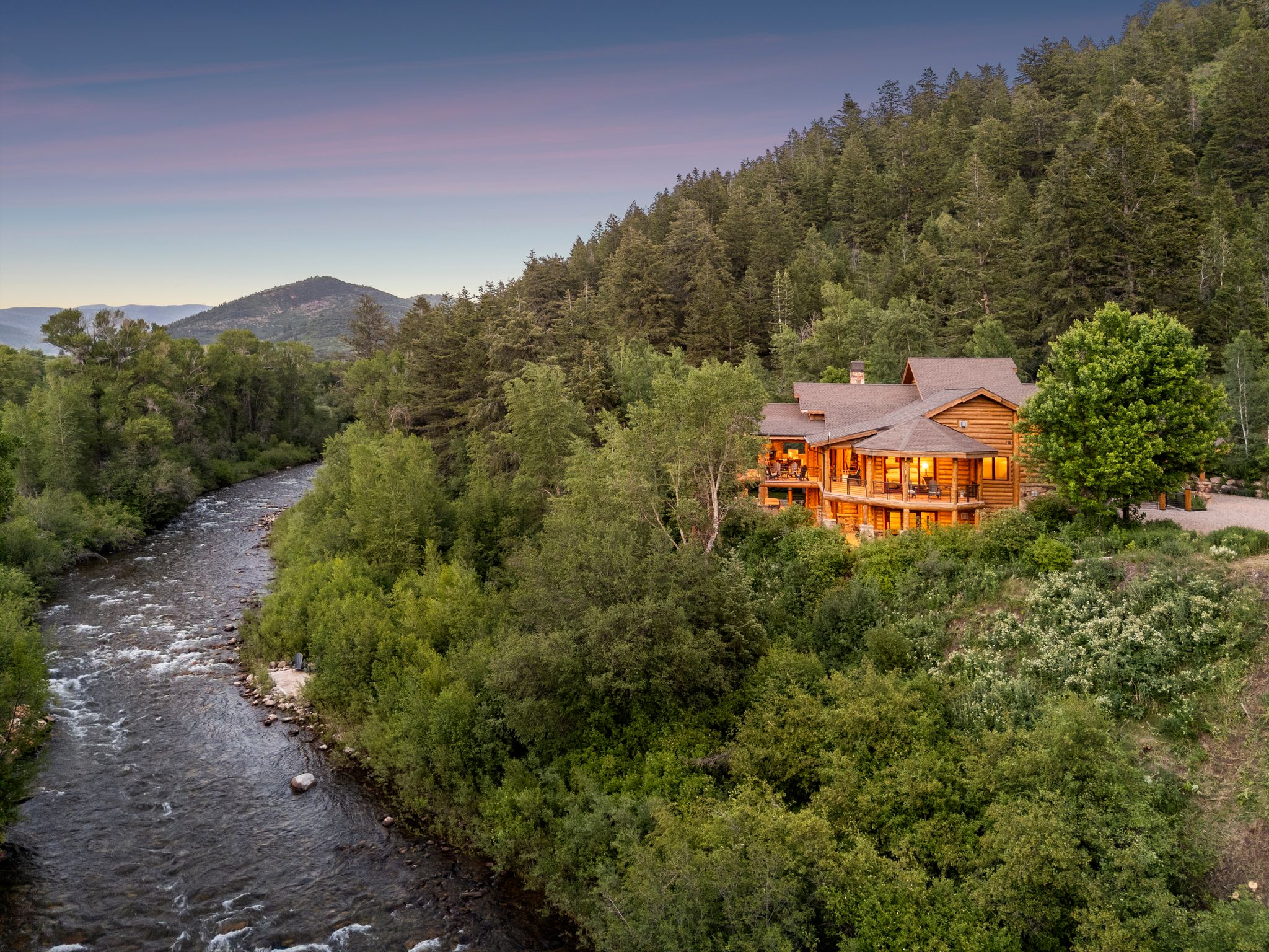 Aerial view at dusk of a split-log veneer framed home, serene river and mountain view