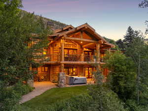 Back of house featuring a hot tub, a balcony, log siding, a patio area, and a chimney