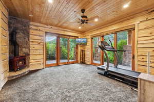 Exercise room featuring wooden ceiling, carpet, recessed lighting, a wood stove, and a ceiling fan