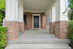 View of exterior entry with brick siding and a porch