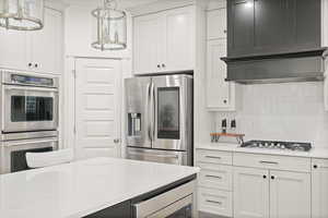 Kitchen featuring stainless steel appliances, tasteful backsplash, white cabinetry, and hanging light fixtures